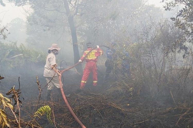Sumarni (kiri) menarik selang untuk melancarkan aliran air dalam upaya pemadaman salah satu titik api di Palangkaraya, Kalimantan Tengah (18/9/2019) 