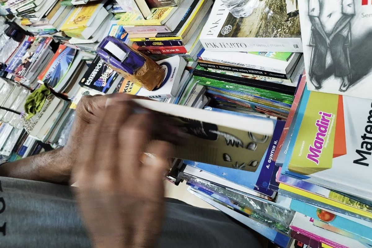 Salah satu pedagang Toko Buku Restu, Fanur (50), sedang membersihkan buku yang hendak dibeli pengunjung, Rabu (01/02/2023). (KOMPAS.com/Xena Olivia)