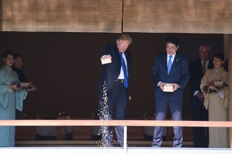 Presiden AS Donald Trump menuangkan seluruh makanan ikan miliknya ke kolam koi disaksikan PM Jepang Shinzo Abe, Senin (6/11/2017).