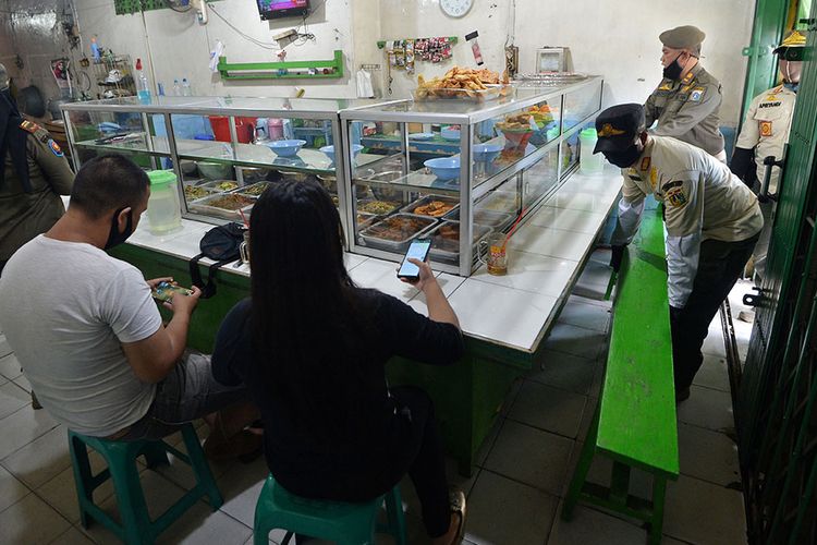 Petugas Satpol PP menertibkan warung makan yang melanggar aturan pembatasan sosial berskala besar (PSBB) di Cililitan, Jakarta, Rabu (29/4/2020). Pelanggaran berupa menerima pelanggan yang makan di warung ditertibkan oleh petugas untuk mencegah penyebaran COVID-19.