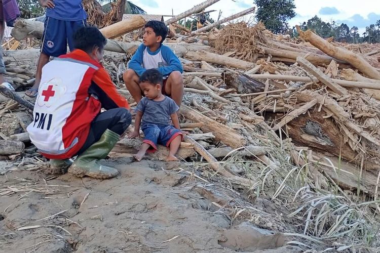 Anak korban banjir bermain bersama relawan disamping tumpukan kayu yang terbawa banjir di Desa Geudumbak, Kecamatan Langkahan, Kabupaten Aceh Utara, Sabtu (3/1/2026).
