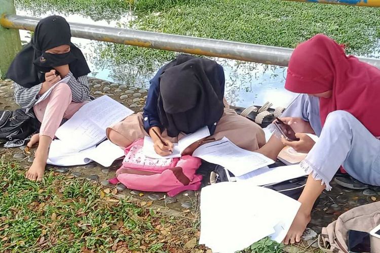 Siswa belajar daring di tepi sungai.