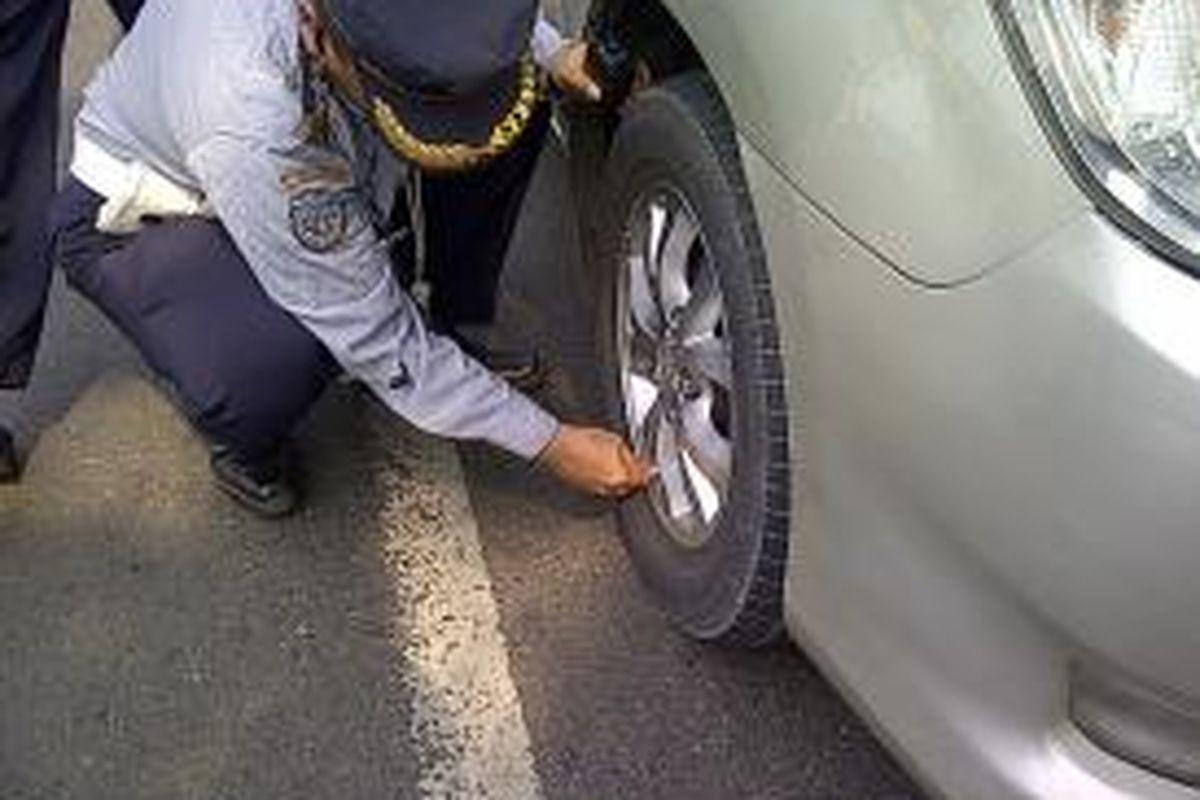 Seorang petugas sedang mencabut pentil ban dan mengempiskannya di Jalan Pemuda, Jumat (27/9/2013). Kendaraan tersebut menyalahi aturan dengan memarkirkan kendaraannya sembarangan.