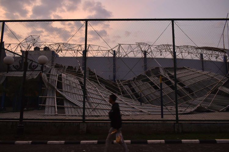 Seorang remaja tengah melewati reruntuhan atap stadion sepakbola SOR Arcamanik yang diterjang hujan disertai angin kencang di Kota Bandung, Sabtu (9/11/2019).