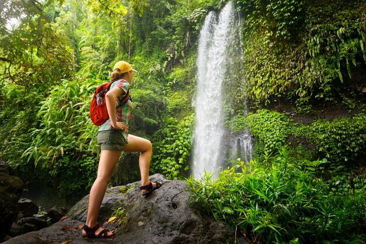 Ilustrasi traveller perempuan sedang mendaki untuk mencapai air terjun. 