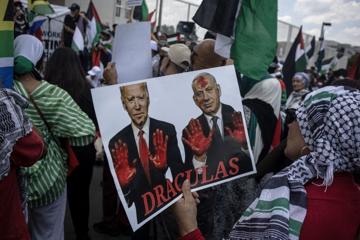 Seorang pengunjuk rasa Pro-Palestina memegang poster bergambar Presiden AS Joe Biden (kiri di poster) dan Perdana Menteri Israel Benjamin Netanyahu (kanan di poster) saat mereka berkumpul di depan Konsulat AS di Sandton, Johannesburg, pada 13 Januari 2024. Ribuan warga sipil, baik warga Palestina maupun Israel, telah tewas sejak 7 Oktober 2023, setelah militan Hamas Palestina yang berbasis di Jalur Gaza memasuki Israel selatan dalam serangan yang belum pernah terjadi sebelumnya yang memicu perang yang diumumkan oleh Israel terhadap Hamas dengan pemboman balasan di Gaza.