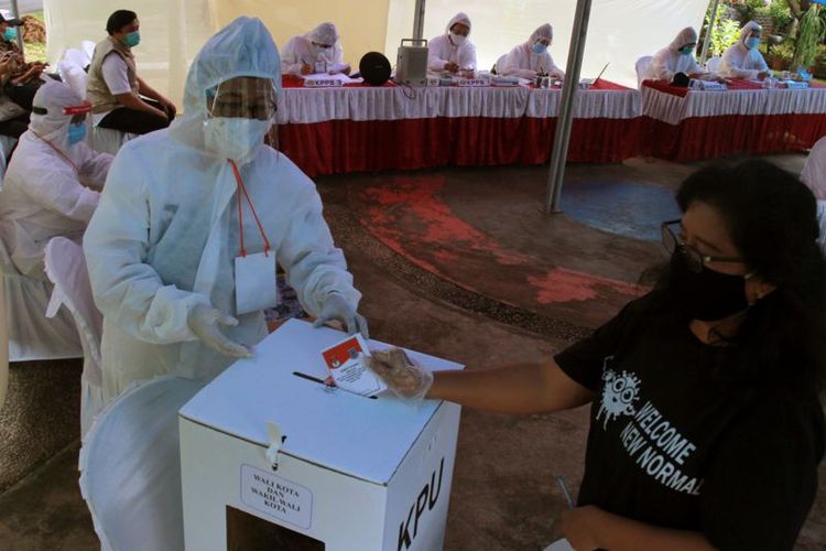 Petugas KPPS berpakaian hazmat mengarahkan pemilih memasukan surat suara ke dalam kotak suara di TPS 46 Paku Jaya, Serpong Utara, Tangerang Selatan, Banten, Rabu (9/12)