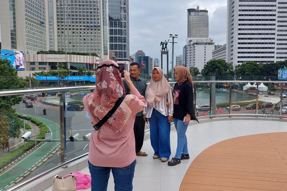 Warga Padang, Sumatera Barat, Julen (46) dan keluarga berfoto dengan latar Bundaran HI dari Halte Tosari, Jakarta Pusat, pada Rabu (28/12/2022).