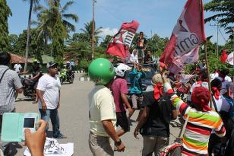 Nampak penyerang menggunakan jaket berwarna hijau sedang mengayungkan kayu ke arah kerumunan massa GMNI