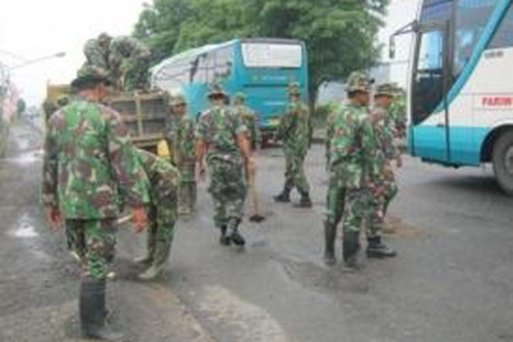Personil TNI menutup lubang jalan pantura dengan batu koral dan padas, Senin (10/2/2014)