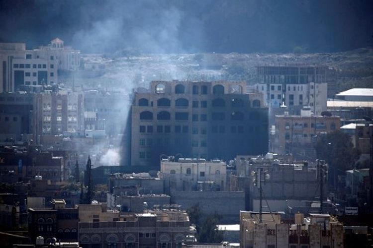 Asap mengepul dari balik gedung di Sanaa, Yaman, pada Minggu (3/12/2017), saat bentrokan terjadi antara kelompok Houthi dan pendukung mantan presiden Yaman, Ali Abdullah Saleh. (AFP/Mohammed Huwais)