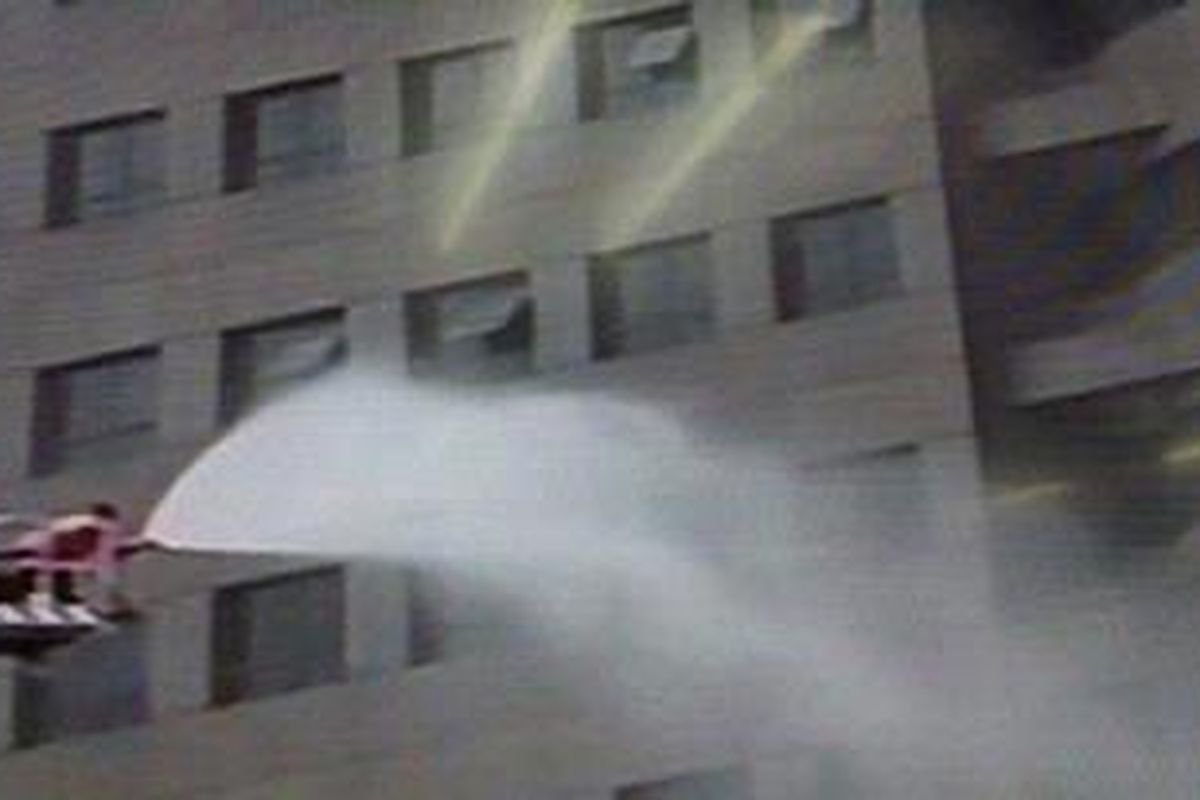 Petugas pemedam kebakaran menyemprotkan air ke Gedung Pusat Pelni yang kebakaran. Seorang pria terjebak.