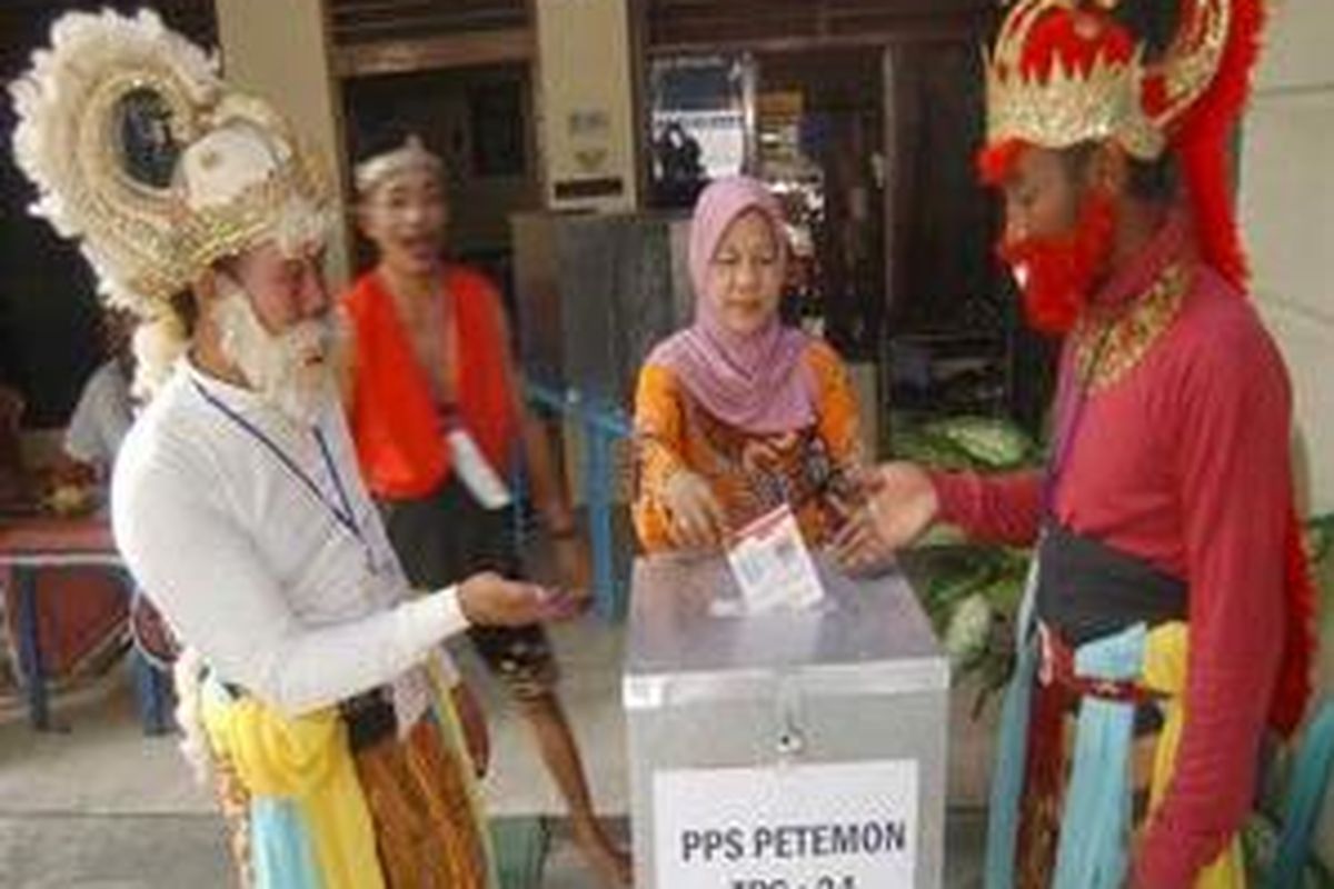 Petugas TPS mengenakan busana tokoh pewayanganuntuk menari minat warga menggunakan hak pilih.