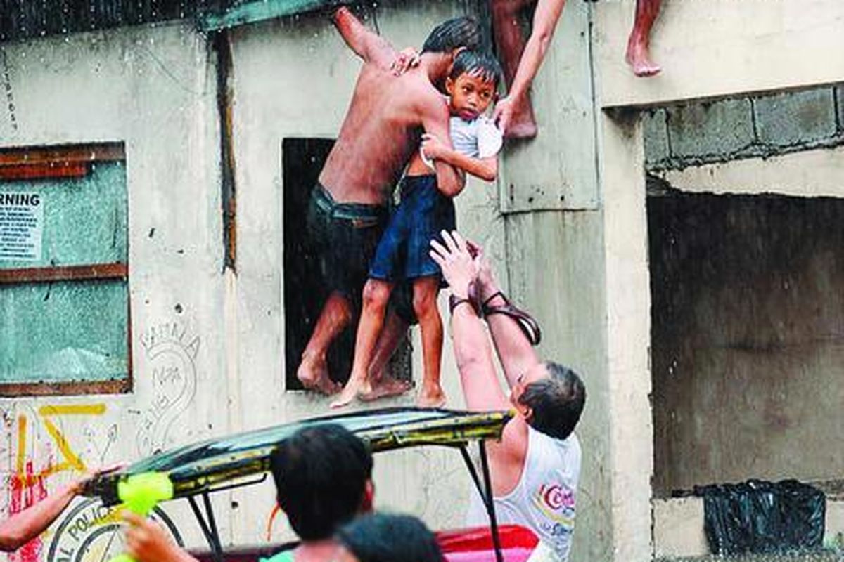 Warga saling menolong untuk mengangkat seorang anak yang terjebak banjir di Quezon City, di pinggiran Manila, Filipina, Sabtu ( 26/ 9) .