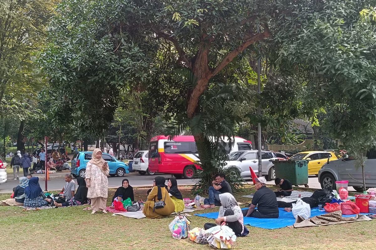Wisatawan piknik di lahan hijau dekat Gedung Elevated Parking di Taman Mini Indonesia Indah, Jakarta Timur, Minggu (25/6/2023).