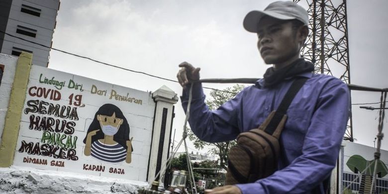 Pedagang yang tidak mengenakan masker berjalan di depan mural yang berisi pesan waspada virus Corona di Petamburan, Jakarta, Rabu (16/09)