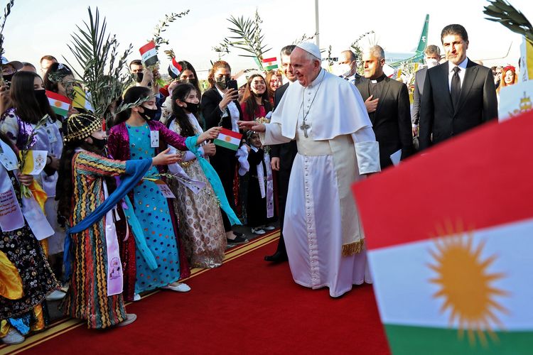 Paus Fransiskus (tengah), ditemani Presiden Region Otonomi Kurdistan Nechirvan Barzani (kanan) menyapa massa yang berpakaian tradisional saat tiba di Bandara Erbil pada 7 Maret 2021. Paus Fransiskus dalam kunjungannya ke Irak, mengunjungi komunitas Kristen yang bertahan di tengah kebrutalan kelompok ISIS di Mosul.