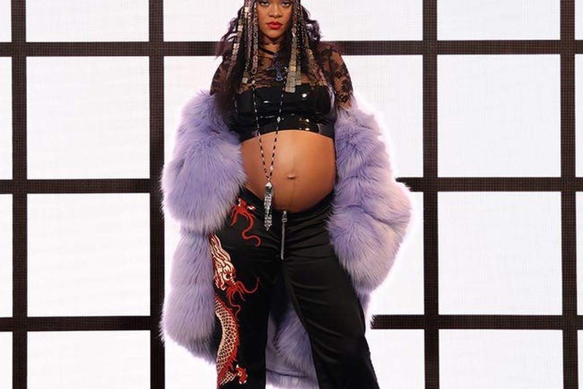 Rihanna mengenakan crop top hitam dan jaket berwarna ungu.