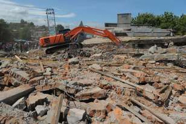 Alat berat digunakan untuk melakukan proses pencarian korban di gedung pertokoan yang roboh akibat terdampak gempa bumi berkekuatan 6,5 skala richter di Pidie Jaya, Aceh, Rabu (7/12/2016). Lebih dari 60 orang tewas dan ratusan lainnya terluka akibat peristiwa ini.