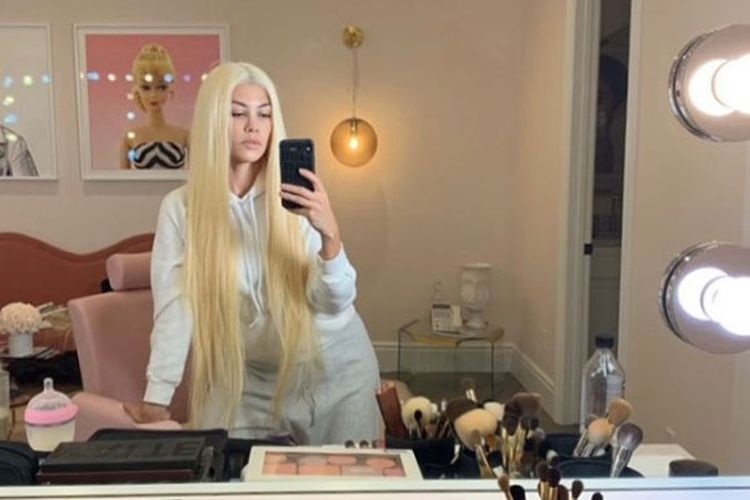 Terlihat pose selfie Kourtney menghadap cermin dengan rambut pirang panjang, dengan gambar Barbie berbingkai di latarnya.