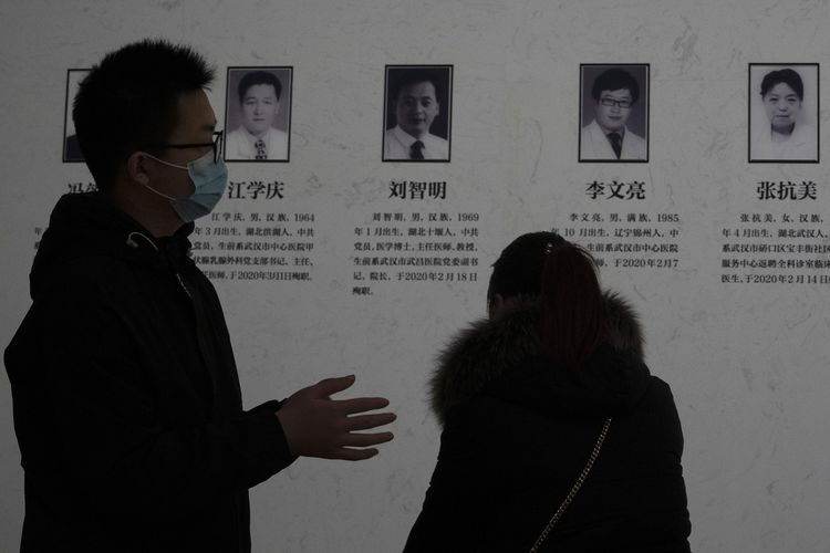 Warga melintas di pajangan yang menampilkan foto para pejuang medis melawan virus corona termasuk whistleblower Dr Li Wenliang (dua dari kanan), di Wuhan, China, pada Sabtu (23/1/2021).