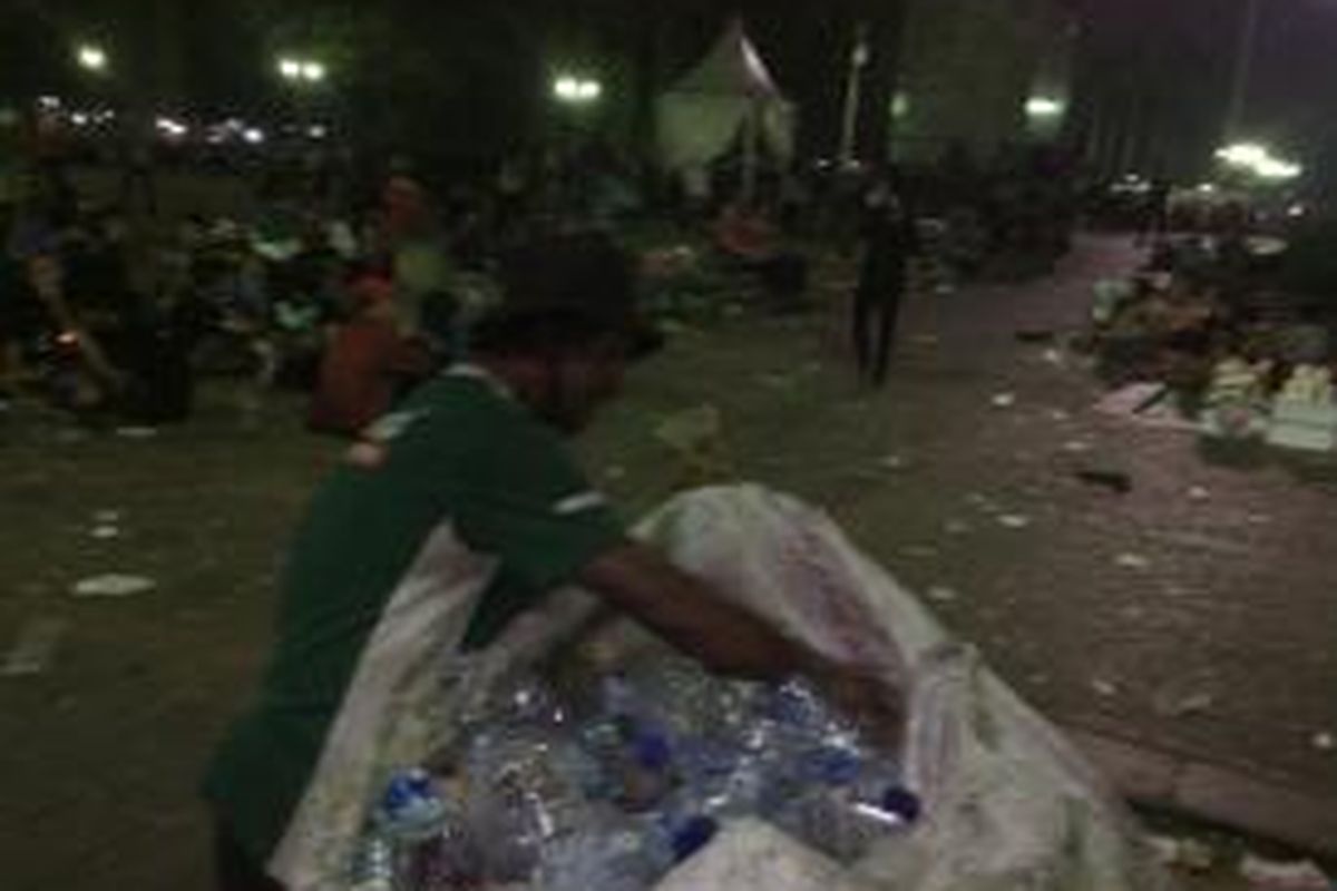 Salah seorang pemulung tengah memunguti sampah botol plastik, usai acara Konser Salam 3 Jari yang berlangsung di Lapangan Monas, Jakarta Pusat, Senin (20/10/2014)
