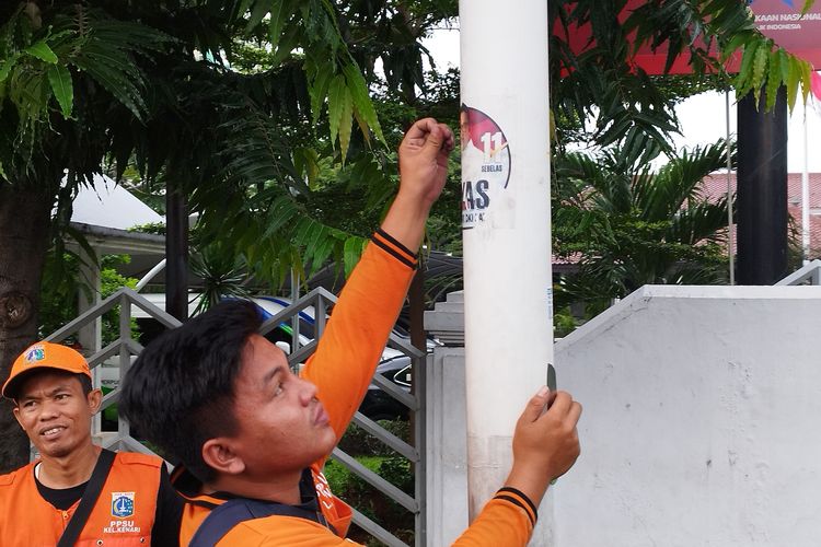 Pasukan oranye mencabut APK yang ditempel di tiang lampu, Jalan Salemba Raya, Senen, Jakarta Pusat, Senin (12/2/2024)