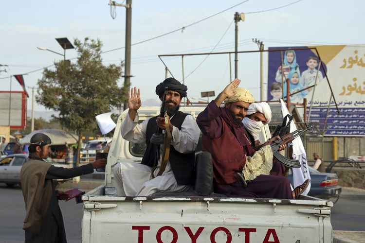 Anggota Taliban melambaikan tangan di belakang truk pikap yang melintas di Kabul, Afghanistan, Senin (30/8/2021).