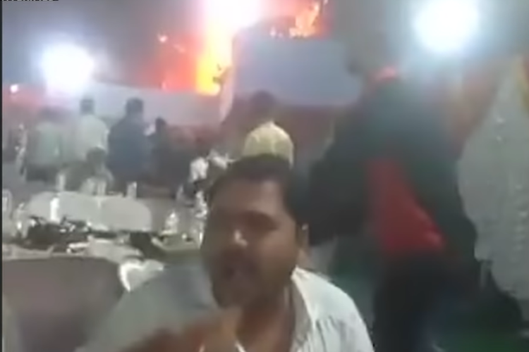 Tangkap layar rekaman, yang difilmkan di Bhiwandi, di Maharashtra, India, dibuka dengan gambar dua pria di meja yang sedang mengobrol santai dengan operator kamera.
