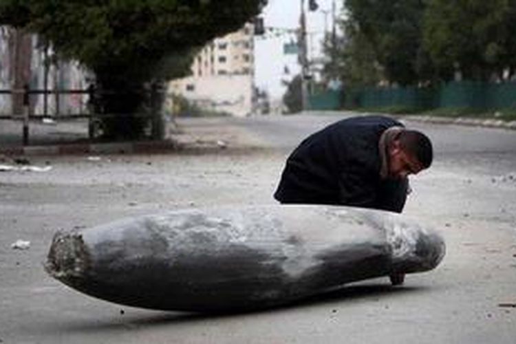 Seorang polisi Palestina mengamati sebuah bom Israel yang jatuh namun tidak meledak di salah satu ruas jalan Gaza City.