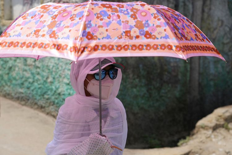 Seorang siswi memegang payung dan menutupi dirinya dengan selendang sebagai pelindung dari sinar matahari di Prayagraj, di negara bagian Uttar Pradesh, India utara, India, Kamis, 21 April 2022.