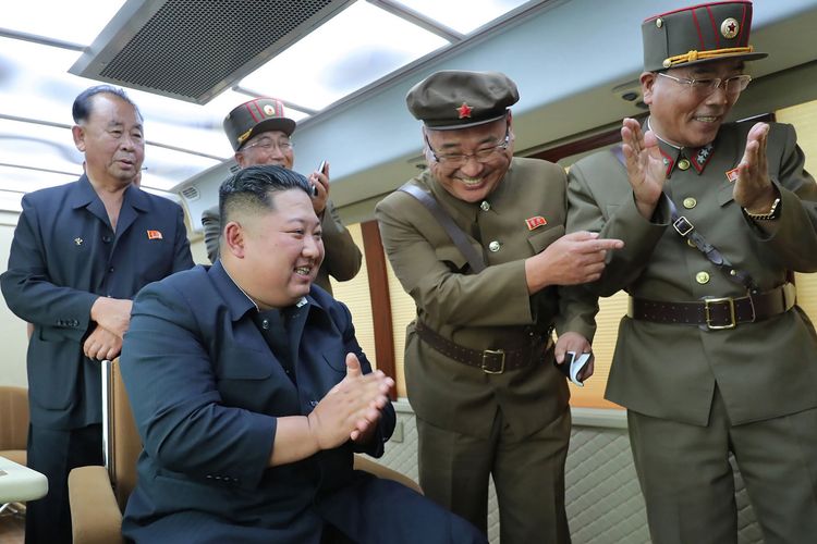 Foto yang dirilis oleh KCNA pada 17 Agustus 2019 menunjukkan Pemimpin Korea Utara Kim Jong Un tersenyum dengan para pejabat militer senior yang mengelilinginya juga tertawa ketika merayakan kesuksesan peluncuran senjata pada Jumat (16/8/2019).
