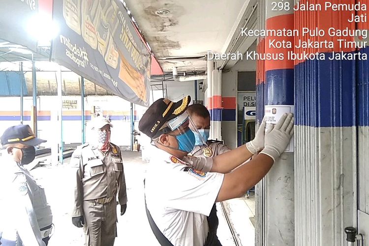 Personel gabungan yang terdiri dari TNI, Polri, Satpol PP, Dinas Perhubungan, dan pihak Kecamatan Pulogadung saat memasang stiker penutupan toko saat PSBB di wilayah Pulogadung, Jakarta Timur, Jumat (17/4/2020).