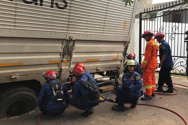 Petugas Suku Dinas Penanggulangan Kebakaran dan Penyelematan Jakarta Timur tengah berupaya evakuasi truk bertonase besar yang amblas di Jalan Komplek PTB Duren Sawit, Jakarta Timur, Selasa (11/2/2020).