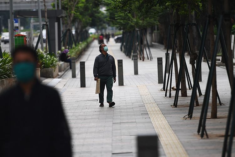 Pejalan kaki melintas di trotoar Jalan Jenderal Sudirman, Jakarta, Selasa (7/4/2020). Pemerintah telah resmi menetapkan Pembatasan Sosial Berskala Besar (PSBB) di wilayah DKI Jakarta dalam rangka percepatan penanganan COVID-19.