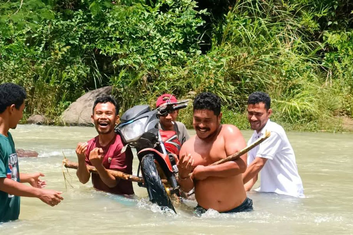 Elvis Jehama, anggota DPRD Manggarai Timur, NTT membantu masyarakat yang sedang menggotong sepeda.motor.saat.menyeberangi DAS Sungai Waemokel di Desa Gunung Baru, Kecamatan Kota Komba, Kabupaten Manggarai Timur, NTT, Sabtu (11/1/2025).