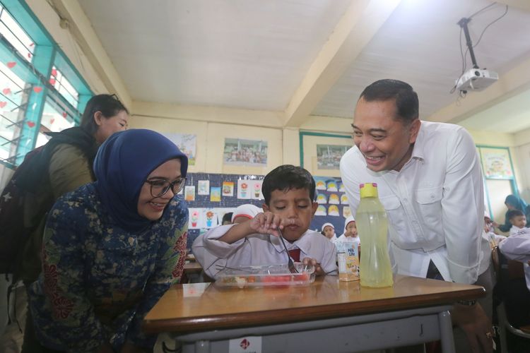 Wali Kota Surabaya Eri Cahyadi memantau langsung pelaksanaan Program Makan Bergizi Gratis (MBG) di salah satu sekolah dasar di Surabaya. Seorang siswa terlihat menikmati makanan sehat yang disediakan dalam program tersebut, sementara Eri memberikan apresiasi terhadap semangat anak-anak.