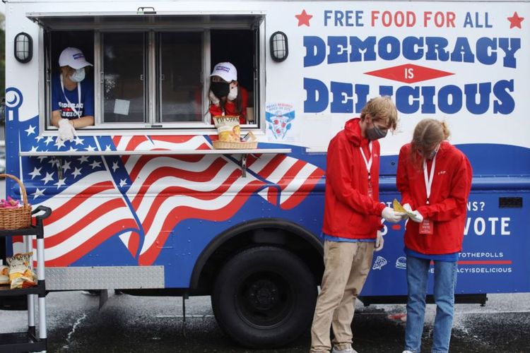 Sejumlah anak muda membagikan makanan dan minuman gratis untuk para pemilih yang mengantre di tempat-tempat pemungutan suara di Charlotte, North Carolina, 29 Oktober 2020.