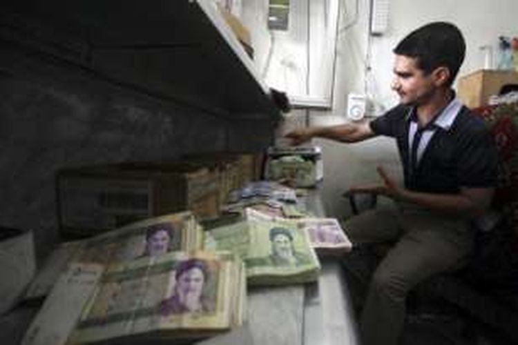 Seorang pria sedang menghitung tumpukan mata uang rial Iran.