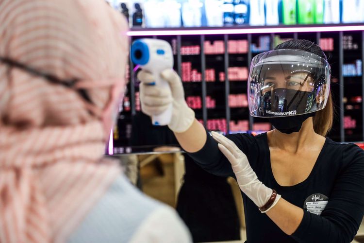 Pekerja salon menggunakan masker dan pelindung wajah, melakukan pemeriksaan suhu tubuh menggunakan thermo gun saat melayani pelanggan.