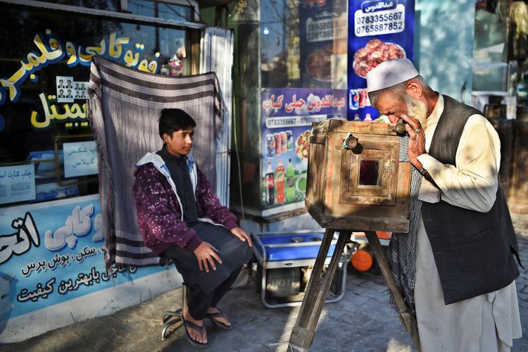 Haji Mirzaman (kanan) mengambil potret seorang anak laki-laki dengan kamera kotak kayu buatannya yang dikenal sebagai kamra-e-faoree di trotoar di Kabul. [WAKIL KOHSAR/AFP]