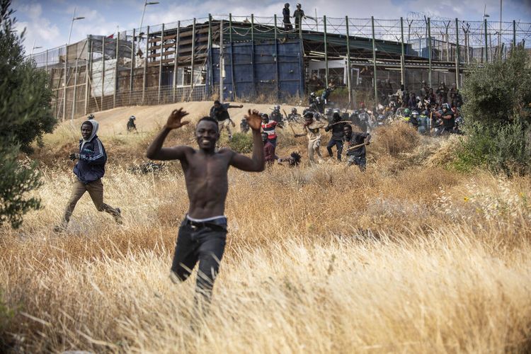 Para migran berlarian di tanah Spanyol setelah melintasi pagar yang memisahkan daerah kantong Spanyol Melilla dari Maroko di Melilla, Spanyol, Jumat, 24 Juni 2022.