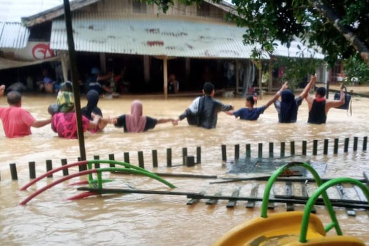 Beberapa warga tampak melintasi banjir di Desa Pelita Sagup Jaya, Kecamatan Indra Makmur, Kabupaten Aceh Timur, Jumat (31/12/2021).