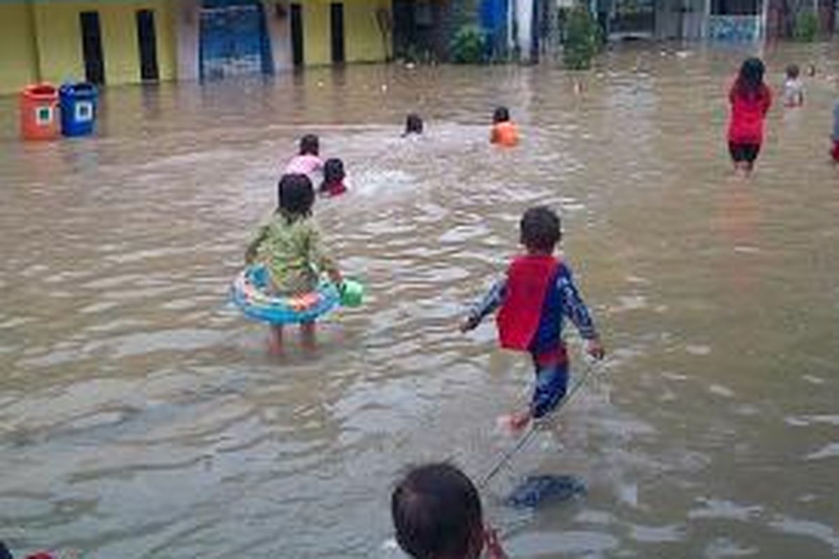 Anak-anak bermain di genangan air depan selter transJakarta Bidara Cina, Jakarta Timur, Minggu (19/1/2014).