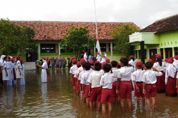 Siswa-siswi SDN Sayung 1 tetap menjalankan upacara bendera meski sekolah mereka masih terendam banjir, Senin (13/2/2017). 
