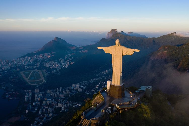 Matahari terbit di hadapan patung Yesus Sang Penebus di Rio de Janeiro pada 24 Maret, 2021. Patung yang berusia 90 tahun tersebut direstorasi sebagai bagian dai perayaan hari jadinya di bulan Oktober 2021. (Photo by CARL DE SOUZA / AFP)