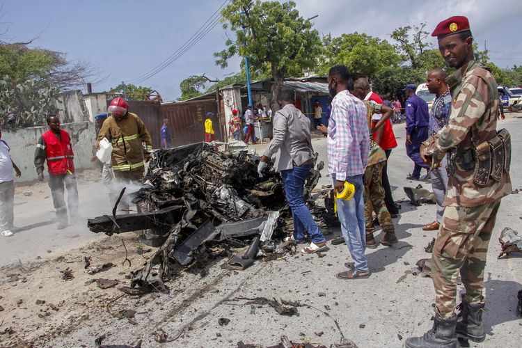 Pasukan keamanan dan warga sipil berdiri di dekat puing-piung setelah serangan bom mobil bunuh diri yang menargetkan komisaris polisi kota di Mogadishu, Somalia, meledak pada Sabtu (10/7/2021). Sedikitnya sembilan orang tewas dan lainnya terluka setelah ledakan besar itu.