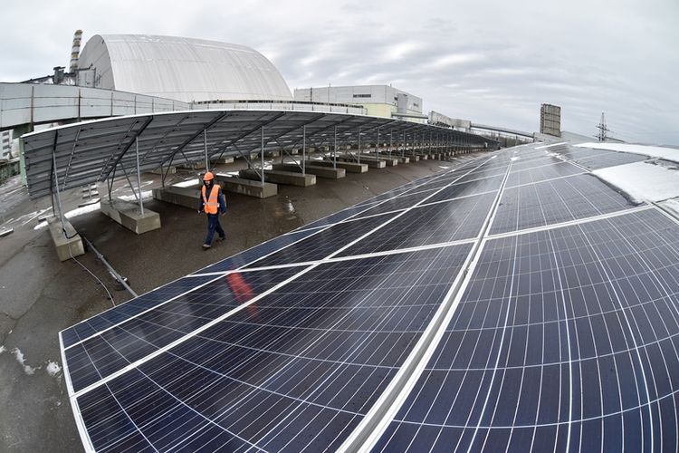 Pekerja melintas di antara panel surya yang telah terpasang di pembangkit tenaga surya Chernobyl, Ukraina. Apa yang dimaksud dengan energi alternatif, energi alternatif adalah, contoh energi alternatif.