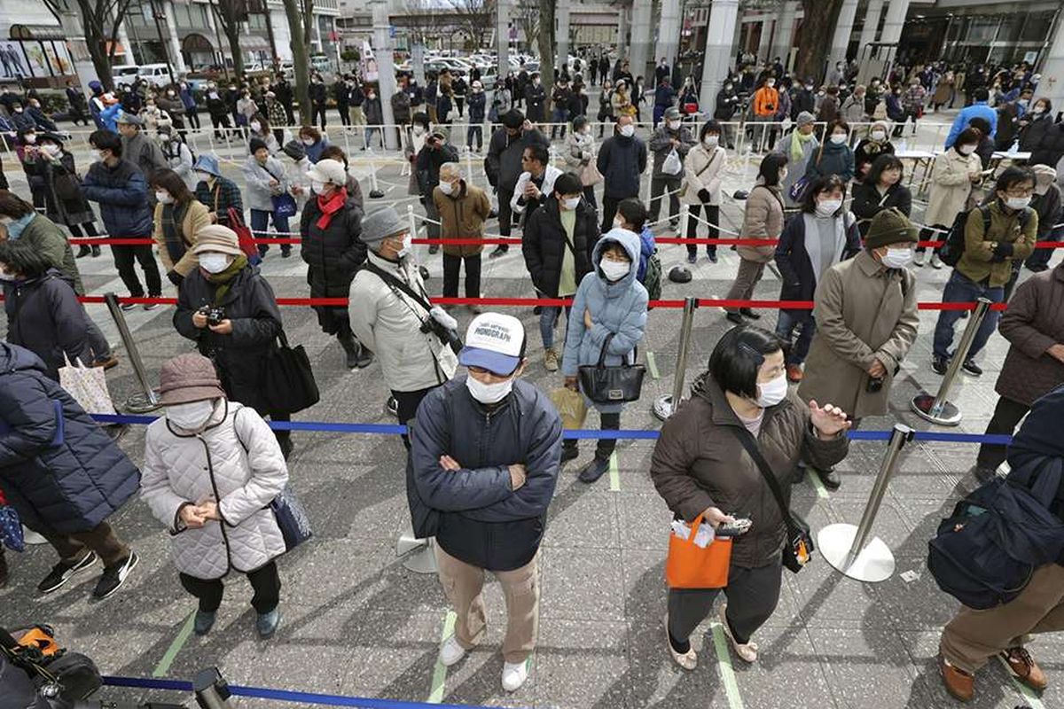 Warga dengan masker pelindung menjaga dari penularan virus COVID-19, mengantre secara berjarak untuk menyaksikan api Olimpiade saat tur Reli Api Olimpiade Tokyo 2020 di Fukushima, Jepang, Selasa (24/3/2020).