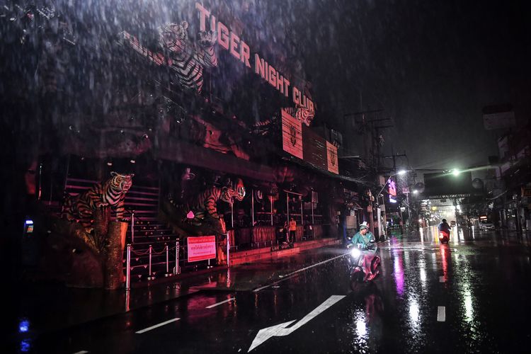 Foto yang diambil pada 1 Oktober 2020 ini menunjukkan orang-orang mengemudi melewati klub-klub kosong di sepanjang jalan pejalan kaki yang populer di Patong di Phuket, yang telah kekurangan wisatawan karena pembatasan yang sedang berlangsung terkait dengan virus corona baru Covid-19. Saat ini, hampir semua 3.000 hotel di pulau itu ditutup dan kota utama Patong telah menjadi kota hantu, kata taipan lokal Preechawut Keesin, yang memiliki lima klub malam dan sekitar 600 kamar hotel, selama wawancara baru-baru ini.